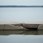 Compromised concrete foundation slab with water seepage near a waterfront, illustrating the impact of bulkhead failure on Lake Conroe properties.