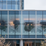 Close-up of a modern mixed-use building's glass-curtain wall structure, highlighting potential cold-bridge condensation issues critical to 'The Uptown Protocol' for Spring mold remediation.