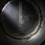 A service technician operates a specialized sprayer, releasing a fine mist into a visible AC duct opening, representing the 'fogging' technique used in some mold removal attempts in Katy, TX.