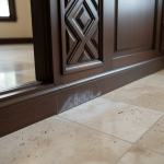 Visible water damage impacting the base of finely crafted Sterling Millwork and adjacent Travertine flooring, demonstrating the specialized challenges of 'moisture clouding' and wood cracking discussed in 'Sterling Millwork & Travertine: Repairing Luxury Finishes After a Flood'.