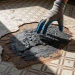 Water-damaged kitchen cabinets removed, exposing dark black mastic adhesive beneath old flooring, a common asbestos risk detailed in 'Repairing Kitchen Cabinets: The Black Mastic Asbestos Risk'.