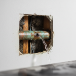 A close-up view of a severely corroded copper pipe with a visible pinhole leak, illustrating the devastating internal damage caused by municipal chloramines, a common issue requiring urgent Houston water damage repair.