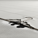 Close-up of commercial VCT tiles with dark, sticky mastic oozing from the seams. This visual represents the advanced stages of VCT tile mastic failure caused by hydrostatic alkalinity, as detailed in the article 'VCT Tile Mastic Failure: Diagnosing Hydrostatic Alkalinity'.