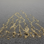 A close-up view of commercial carpet tiles displaying distinct yellow-brown bitumen bleed stains caused by water damage.