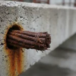 Close-up of a severely corroded post-tension cable or rebar protruding from a cracked concrete slab, illustrating typical foundation damage from post-tension cable corrosion.