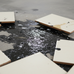 Detailed view of commercial VCT tiles with black mastic oozing from seams, a clear sign of alkalinity and moisture-driven failure requiring urgent assessment.